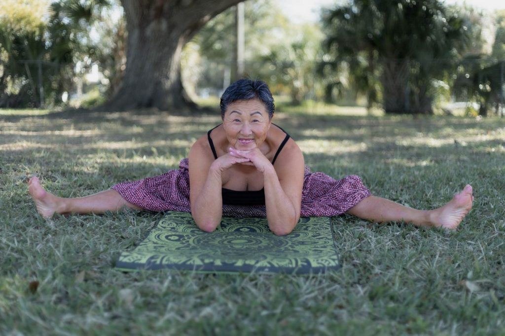 Senior woman performing yoga stretches in a sunny park setting, radiating health and vitality.
