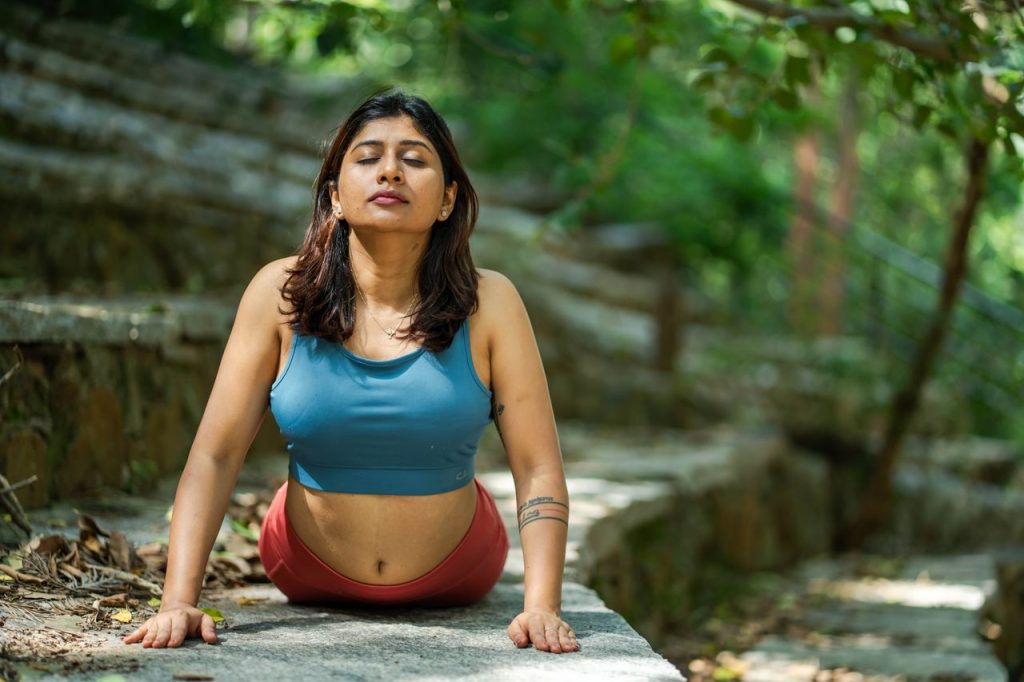 Adult woman engaging in outdoor yoga meditation, surrounded by lush greenery. Calm and peaceful setting.